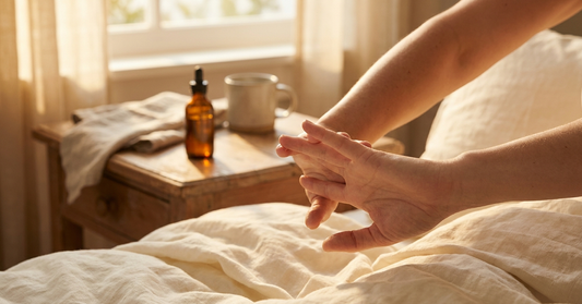 Relaxed hands stretching gently in warm morning light with an amber tincture bottle on a wooden bedside table