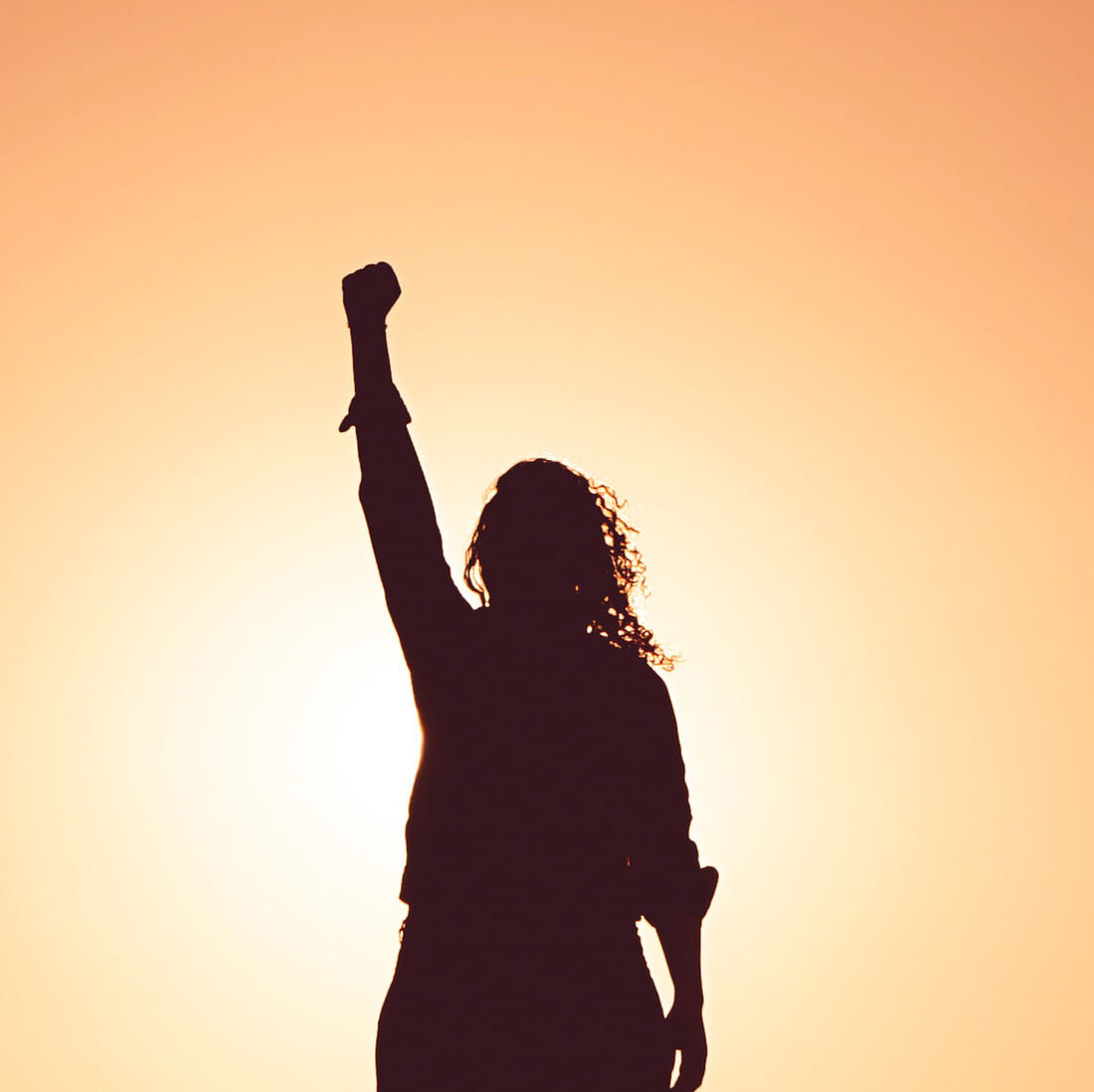 Woman raising her hand towards the sky in the sunset.