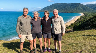 A group of four adults aged 50 to 70 smiling together on a headland above the Far North Queensland coast