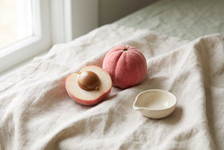 Ripe pink blushwood berry whole and cut in half showing the large brown seed inside, on natural linen