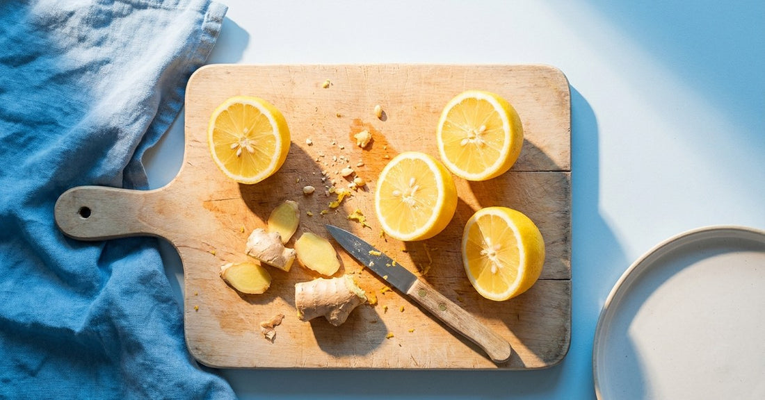 An overhead shot of a wooden chopping board with halved lemons and a peeled ginger root, raking morning light, citrus-yellow and white palette. ENERGY palette.