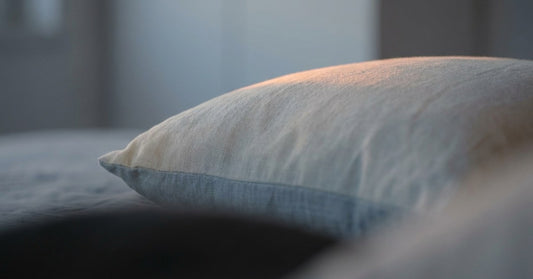 The curve of a single pillow under cool blue-grey dawn light with one warm sliver of sunrise creeping across the top edge, extreme shallow depth of field. DAWN palette.
